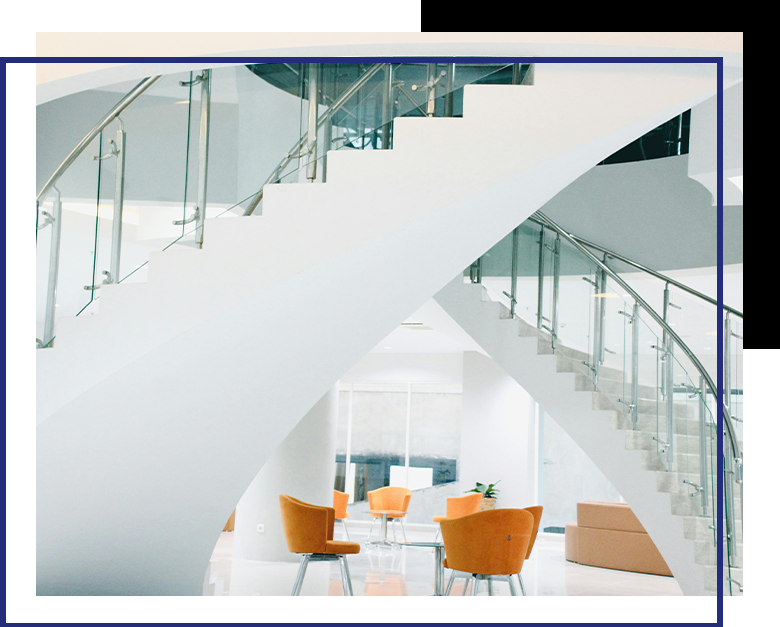 A sleek, modern staircase with glass railings curves through a bright, open lobby furnished with contemporary orange chairs.